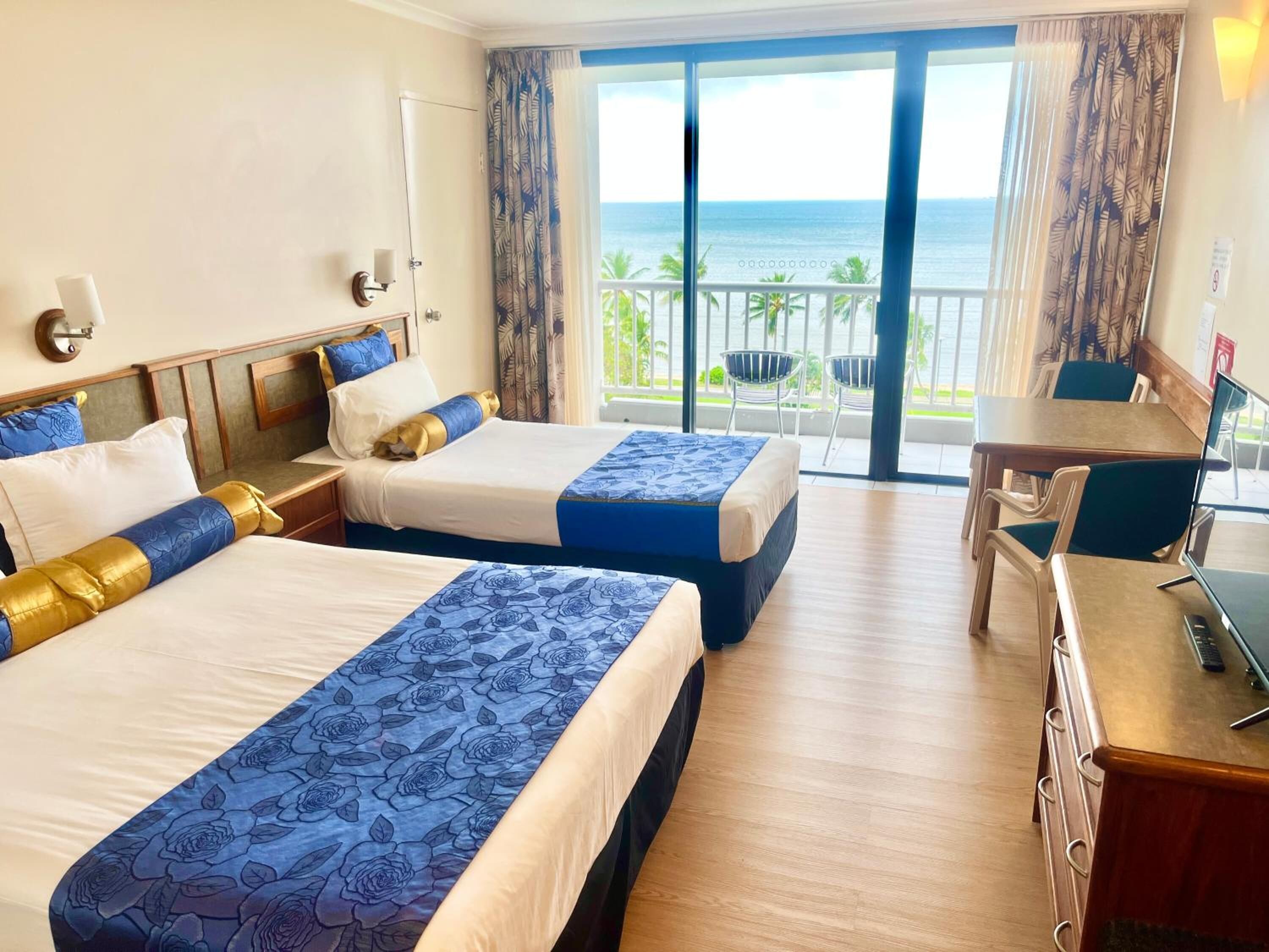Habitación de hotel con dos camas, un escritorio y un balcón con vistas al mar.