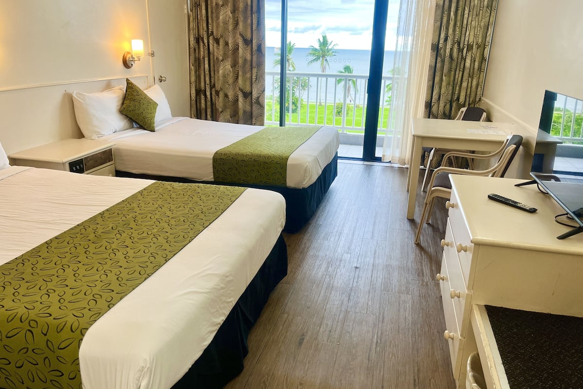 A hotel room with two beds, a desk, and a view of the ocean.