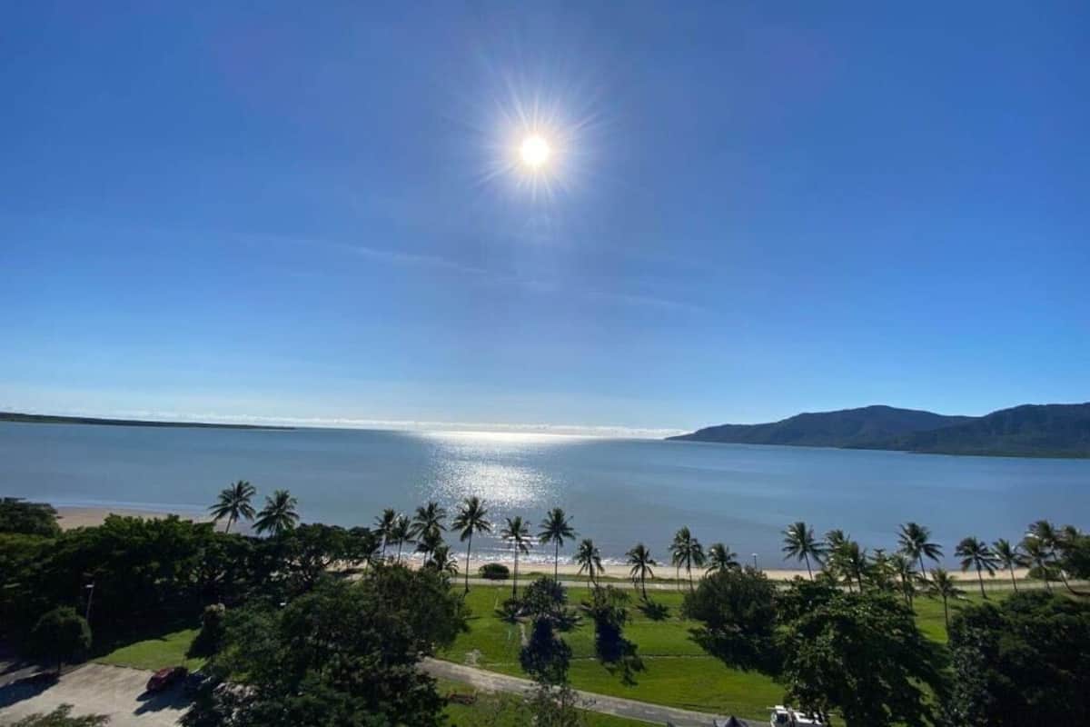 A coastal view with a clear sky, calm sea, and palm trees.