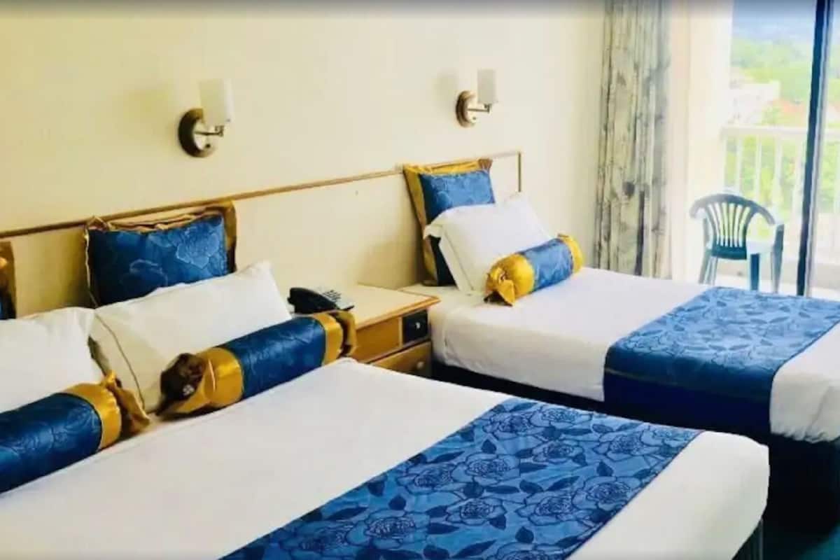 Two beds with blue and white bedding, a nightstand, a chair, and a balcony with a view.