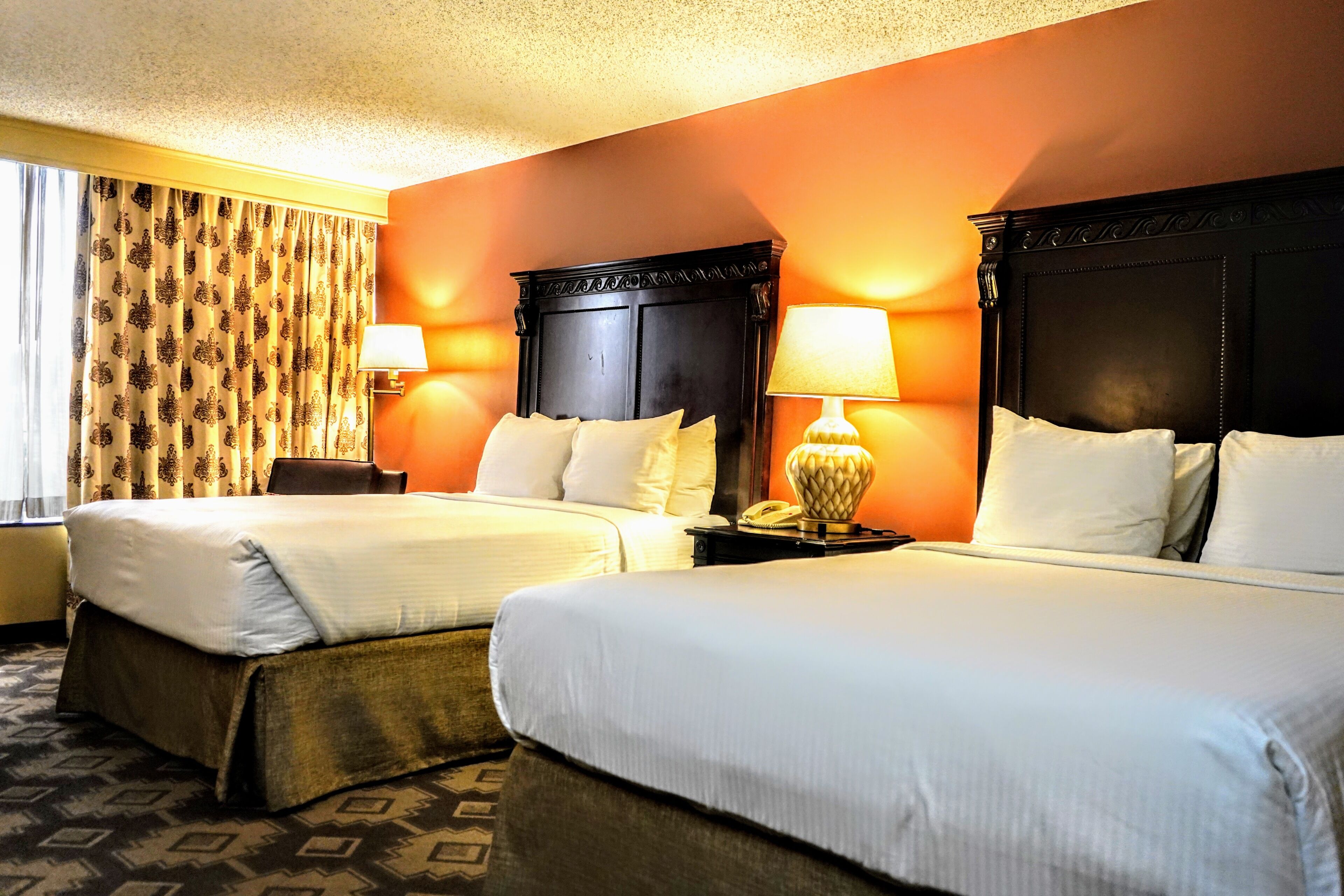 A hotel room with two beds, a patterned curtain, a lamp, and a telephone on the nightstand.