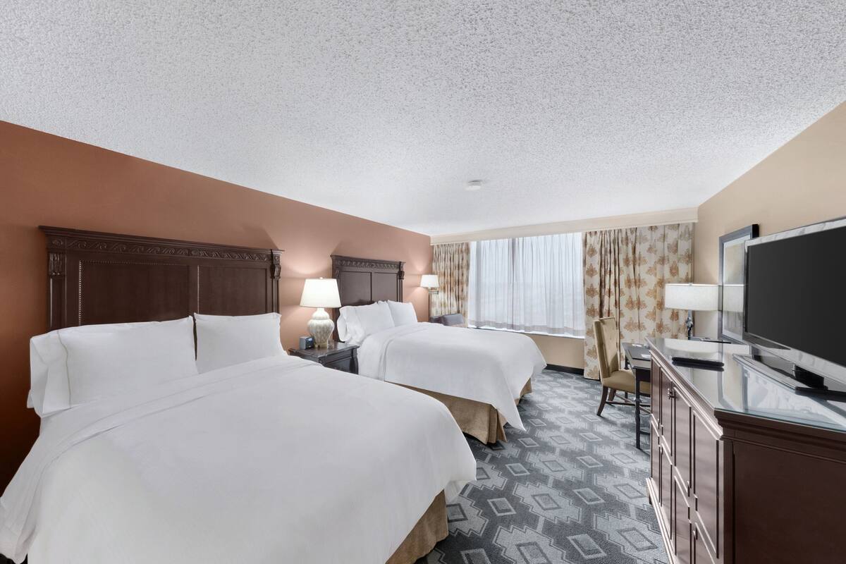 A hotel room with two beds, a TV, a desk, and a chair.