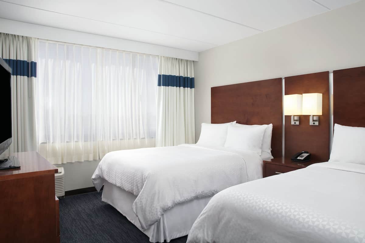 A hotel room with two beds, a TV, a desk, and a nightstand with a lamp.