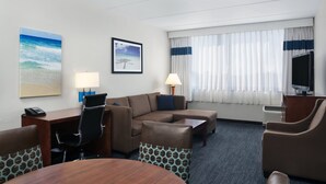 A hotel room with a sofa, armchairs, a desk with a phone, a TV, and a large window with curtains. - Four Points by Sheraton Fort Lauderdale Airport/Cruise Port (Fort Lauderdale)