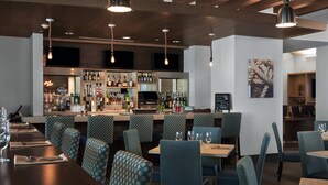 A restaurant with a bar area, seating with patterned chairs, and a variety of bottles on shelves. - Four Points by Sheraton Fort Lauderdale Airport/Cruise Port (Fort Lauderdale)