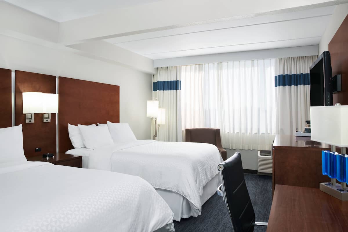 A hotel room with two beds, a desk, a chair, a TV, and a window with curtains.