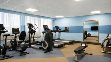 Une salle de sport équipée de vélos d’appartement, de tapis de course et d’un banc de musculation.