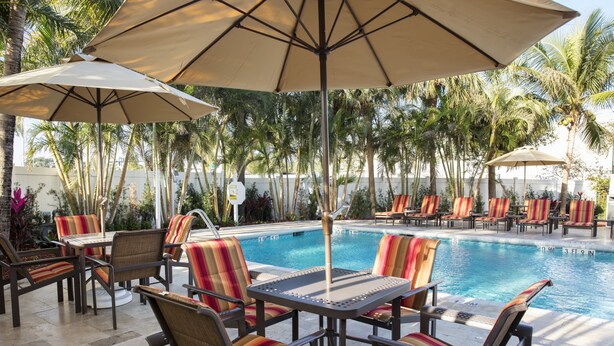 A poolside area with lounge chairs and umbrellas, surrounded by palm trees. - Four Points by Sheraton Fort Lauderdale Airport/Cruise Port (Fort Lauderdale)