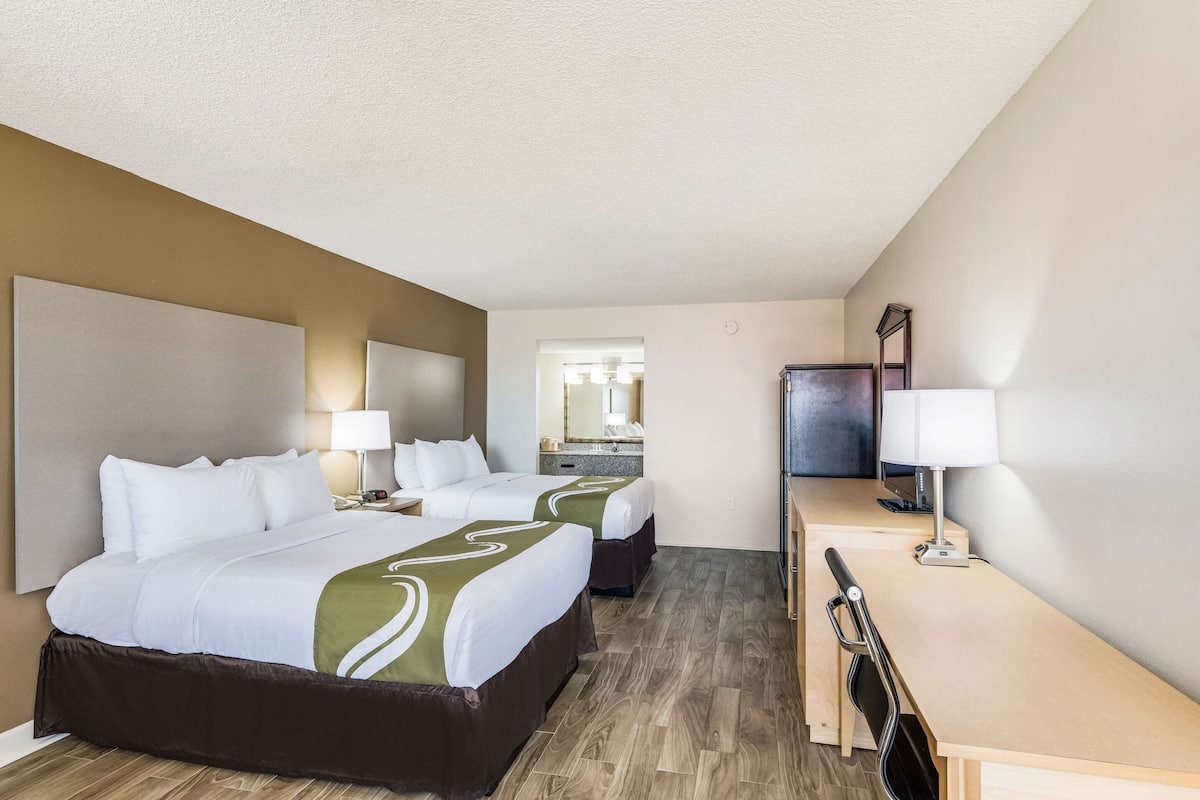 A hotel room with two beds, a desk, a chair, a TV, and a mirror.