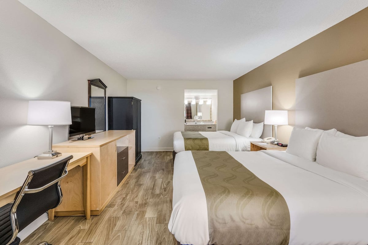 A hotel room with a desk, two beds, a mirror, and a TV.