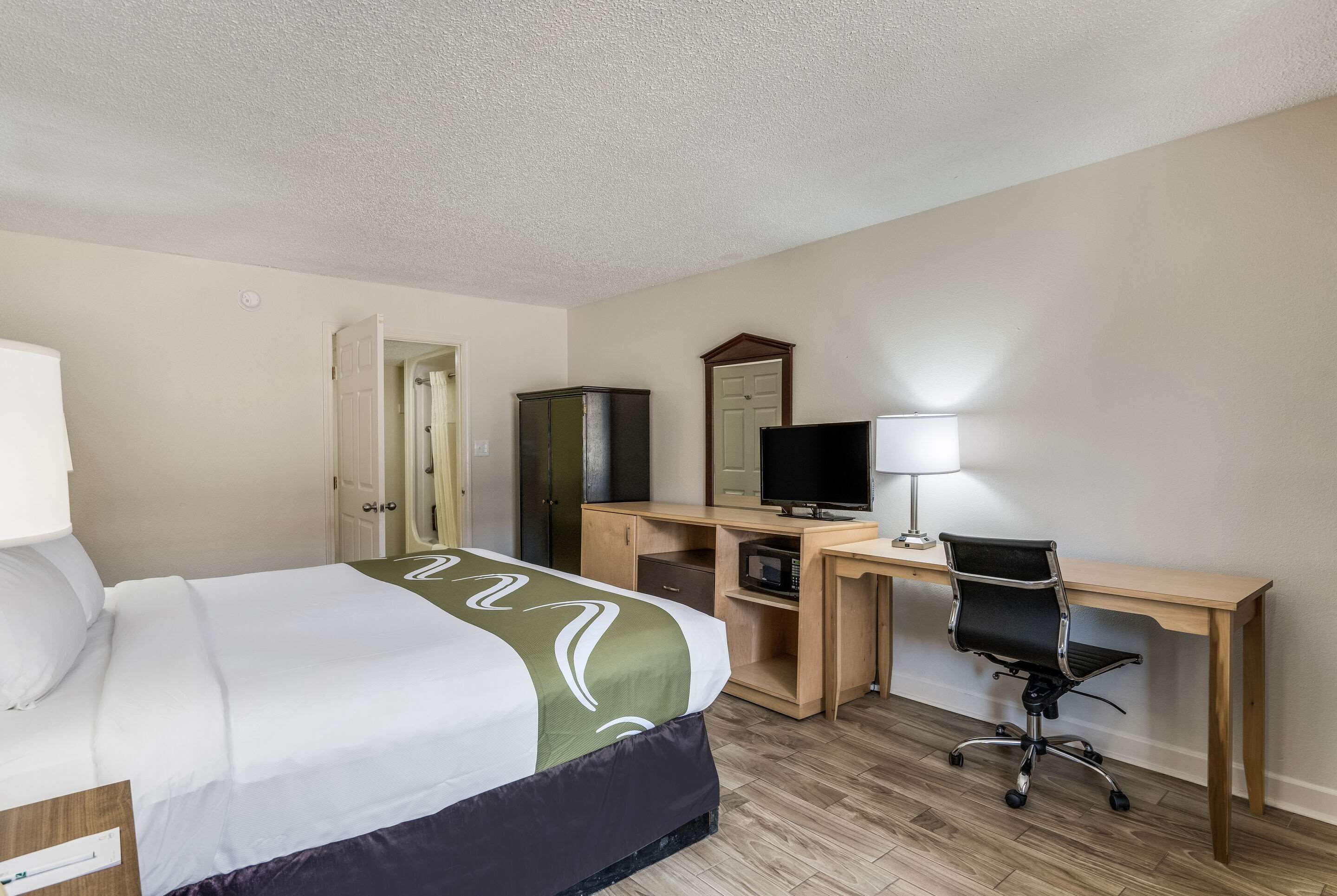 A hotel room with a bed, desk, chair, television, and a mirror.