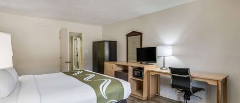 A hotel room with a bed, desk, chair, television, and a mirror.