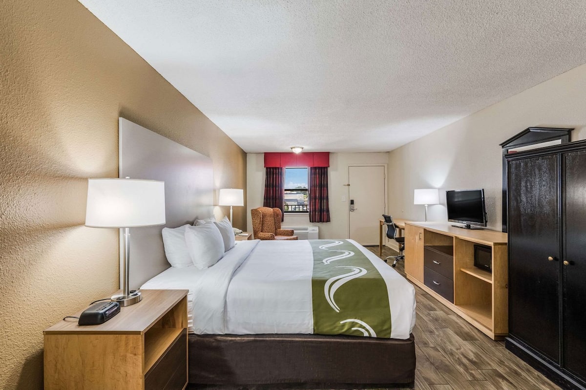 A hotel room with a bed, desk, TV, wardrobe, and a view of the outside.
