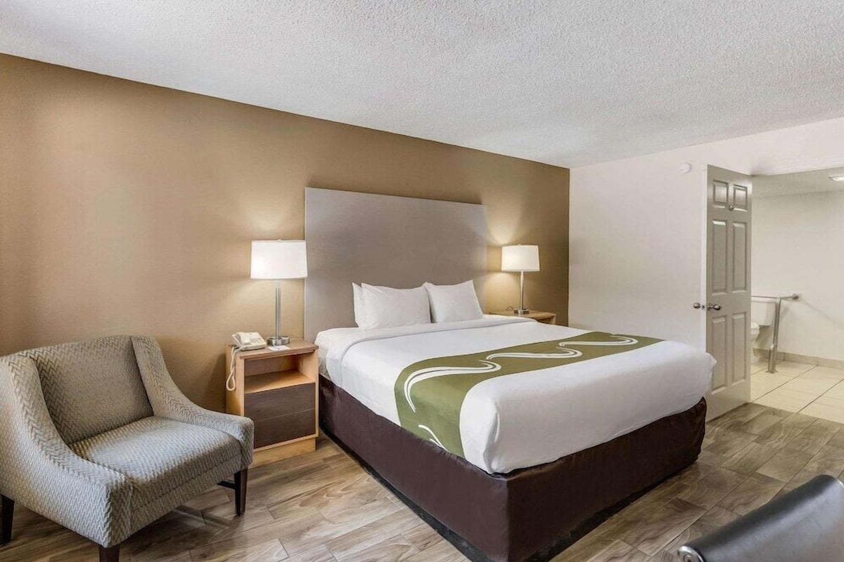 A hotel room with a bed, bedside lamps, a chair, a nightstand, and a door.