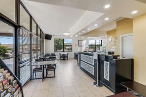 A modern hotel lobby with a reception desk, seating area, and large windows offering views of the outside.