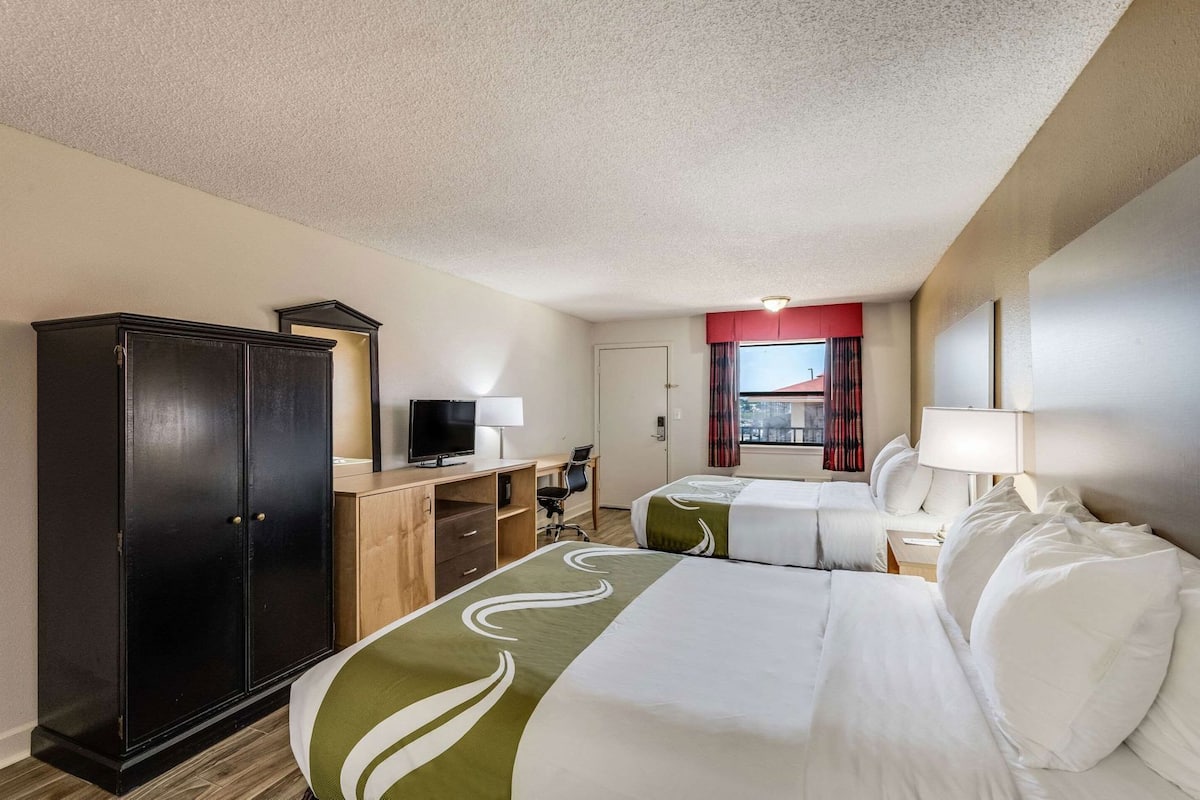 A hotel room with a bed, a desk with a computer, a wardrobe, and a window with curtains.