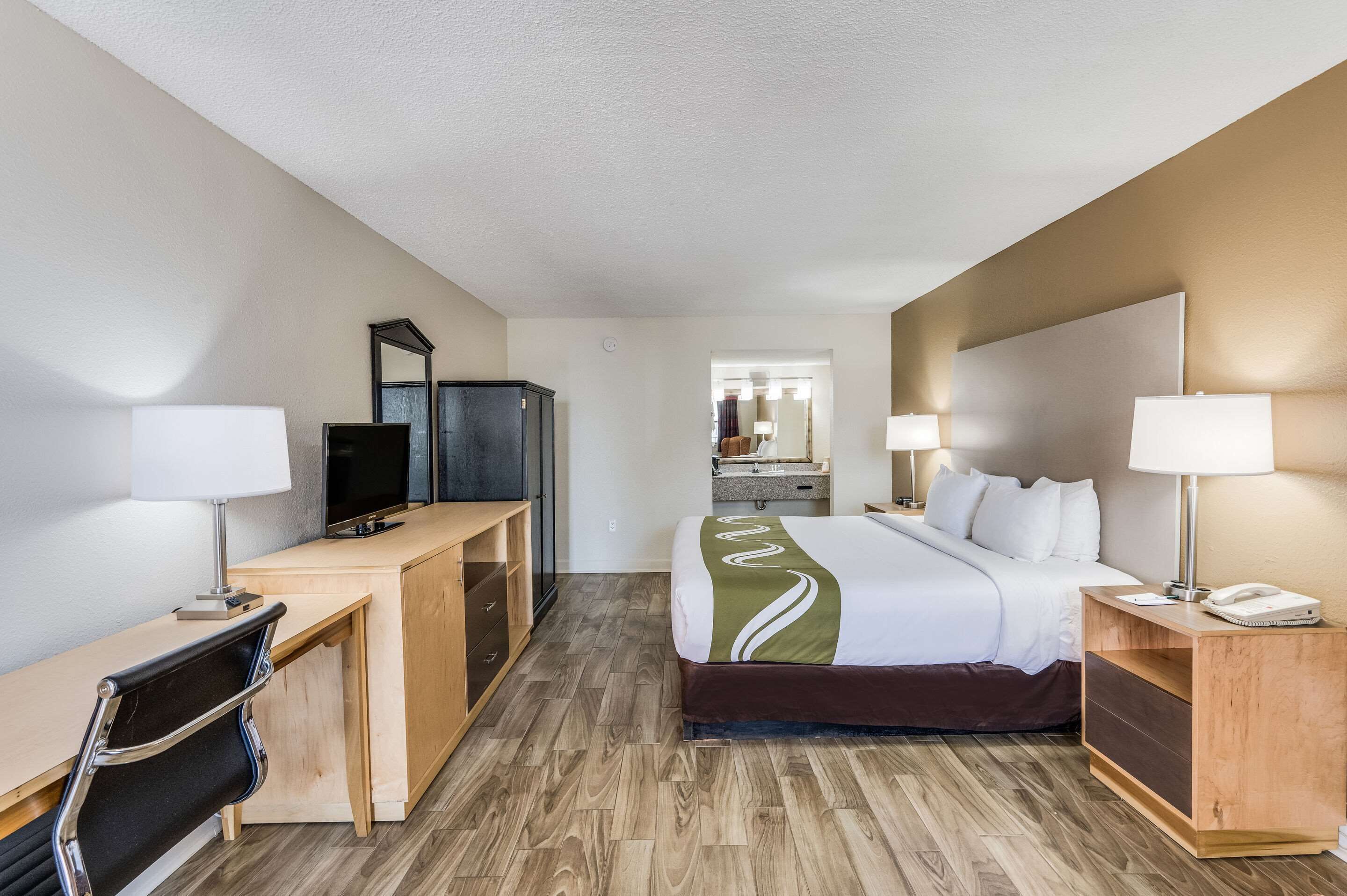 Una habitación de hotel con cama, escritorio, silla, televisión y espejo.