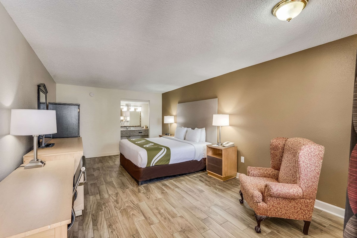 A hotel room with a bed, bedside lamps, a chair, a desk with a lamp, and a television.