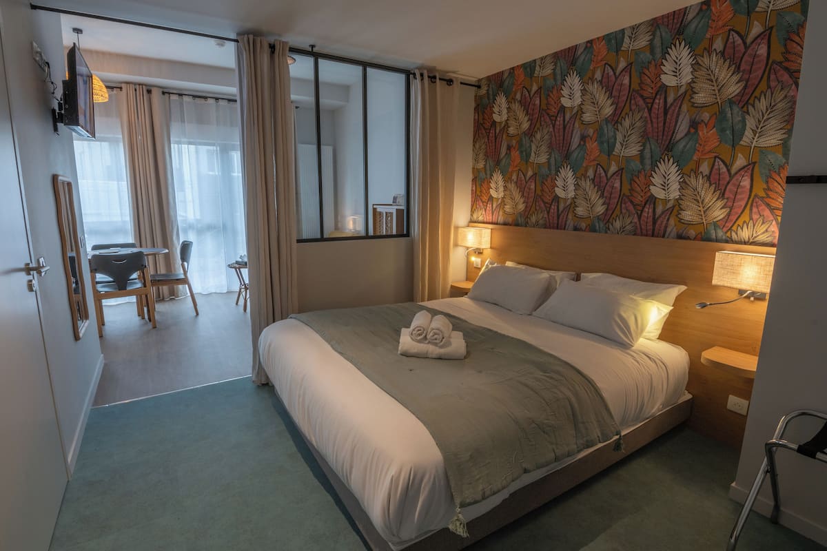 Ein Hotelzimmer mit einem großen Bett, einem Schreibtisch mit Stuhl, einem kleinen Tisch und einem Spiegel.