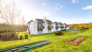 A row of modern, white buildings with multiple balconies, set in a green landscape with a clear sky. - The Originals City, Ara Hôtel (Landerneau)