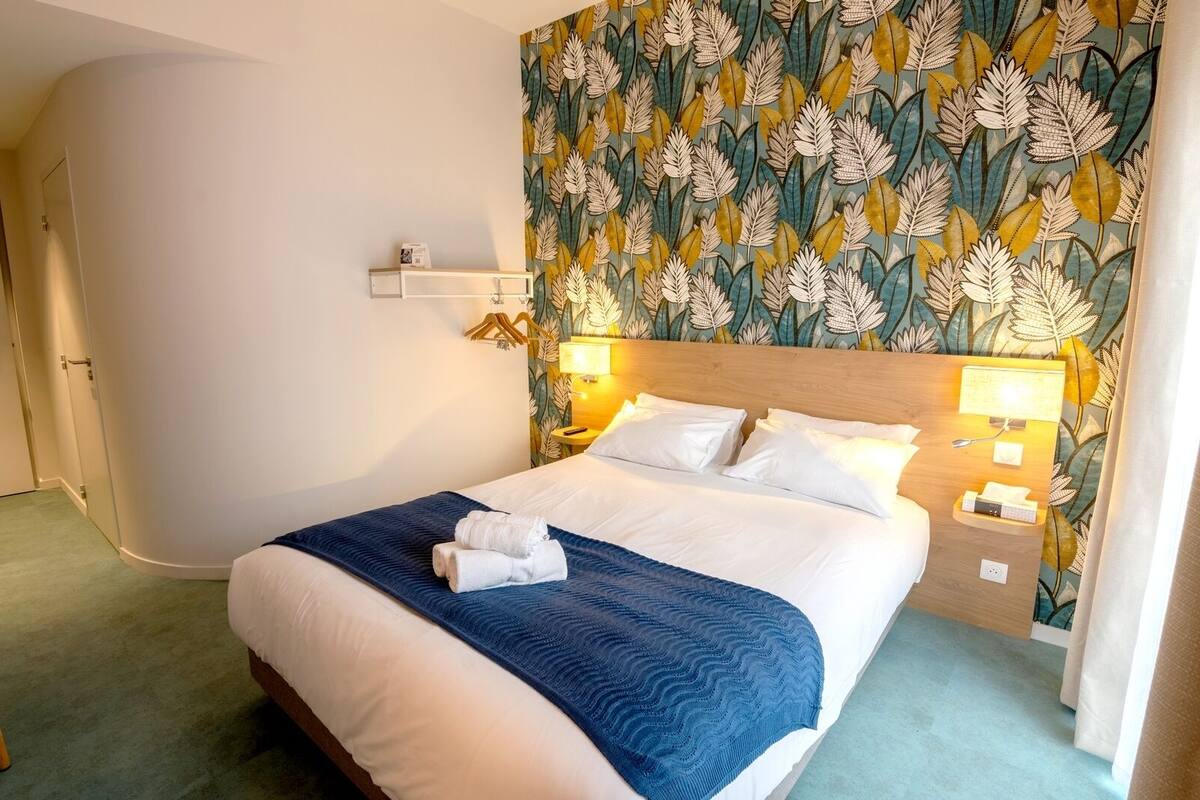 Ein Hotelzimmer mit einem großen Bett, einem blumengemusterten Kopfteil, Nachttischlampen und einer blauen Tagesdecke.