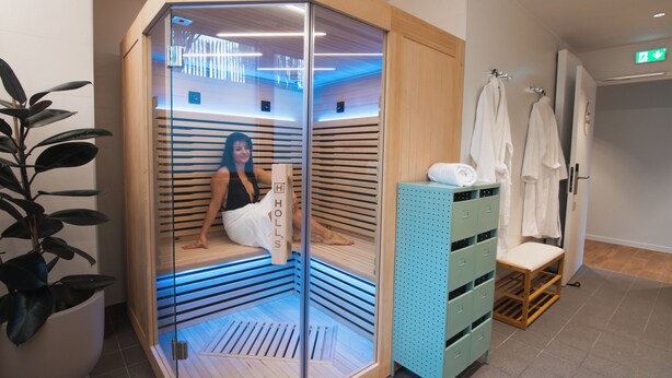 A sauna room with a glass enclosure, a wooden bench, and a towel rack with towels. - The Originals City, Ara Hôtel (Landerneau)