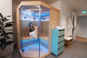A sauna room with a glass enclosure, a wooden bench, and a towel rack with towels.
