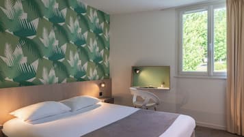 Habitación de hotel con cama, escritorio con silla, ventana con cortinas y pared con diseño de hojas.