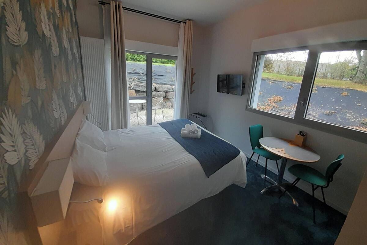 Ein Hotelzimmer mit Bett, kleinem Tisch mit Stühlen, Fernseher und Fenster mit Blick nach draußen.
