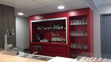 Zona de bar con estantes llenos de botellas de licor y vasos, una cafetera y un lavabo.