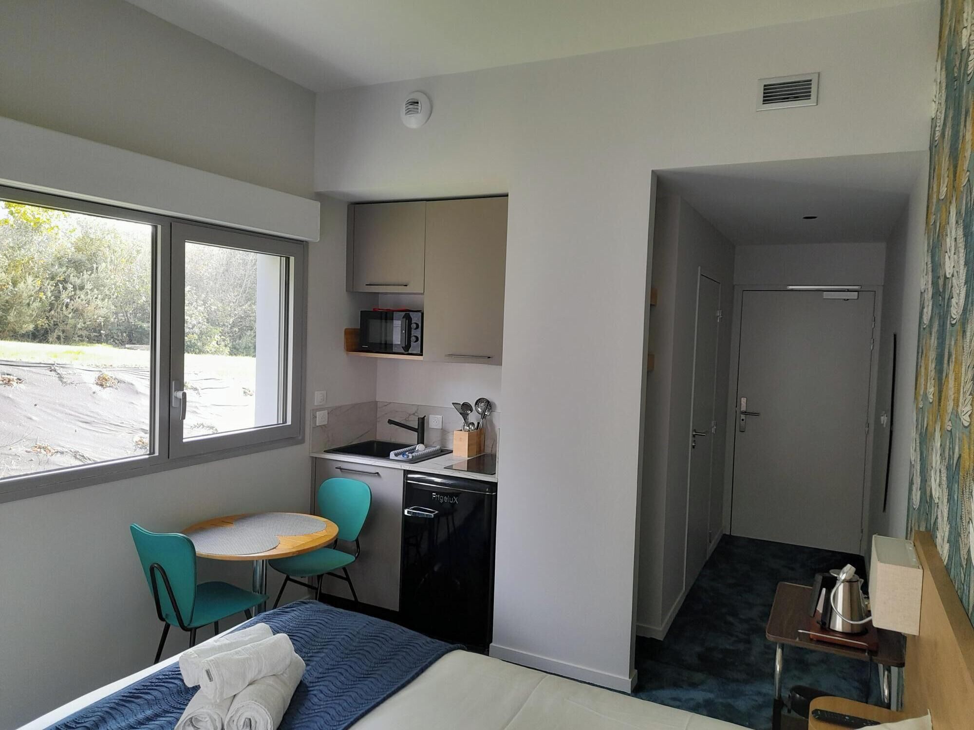 A compact hotel room with a bed, a small kitchenette, a dining area, and a bathroom.