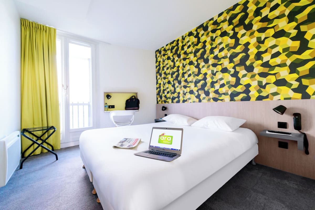 Ein Hotelzimmer mit Bett, Laptop, Schreibtischlampe, Telefon und Wand mit geometrischem Muster.
