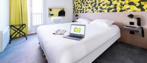 A hotel room with a bed, a laptop, a desk lamp, a telephone, and a wall with a geometric pattern.