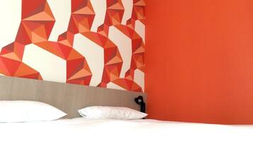 Une chambre d’hôtel avec un mur orné d’un motif géométrique, une tête de lit en bois et un lit avec une literie blanche.