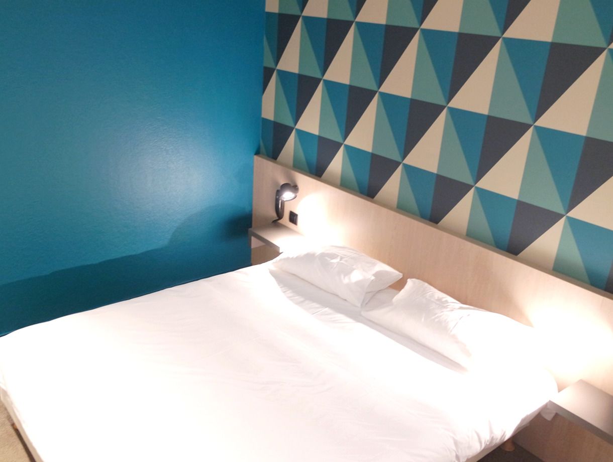 Habitación de hotel con cama, mesita de noche y pared con diseño geométrico.