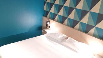 Habitación de hotel con cama, mesita de noche y pared con diseño geométrico.
