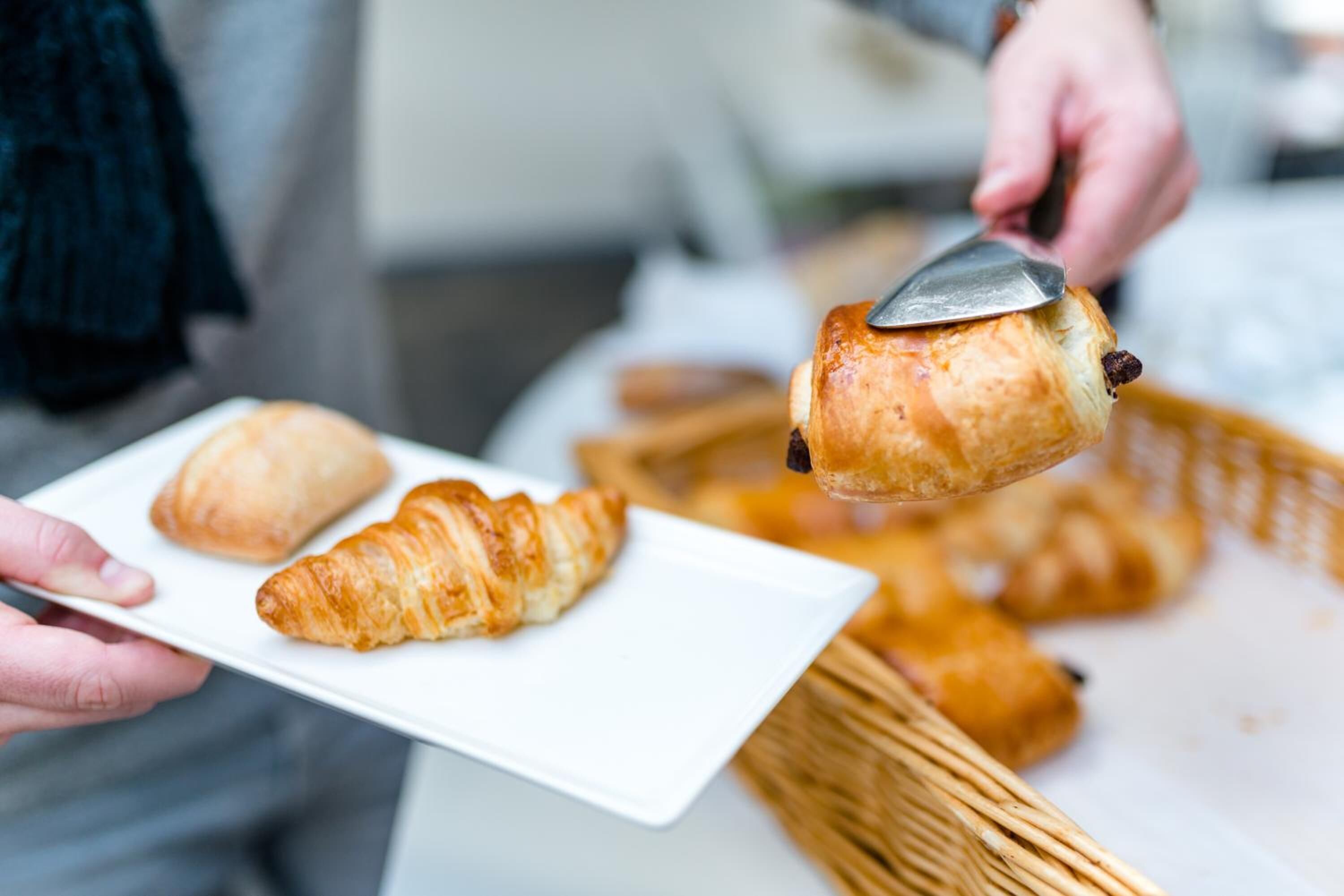 Una persona sosteniendo un plato con dos croissants y un pastel con una cuchara.