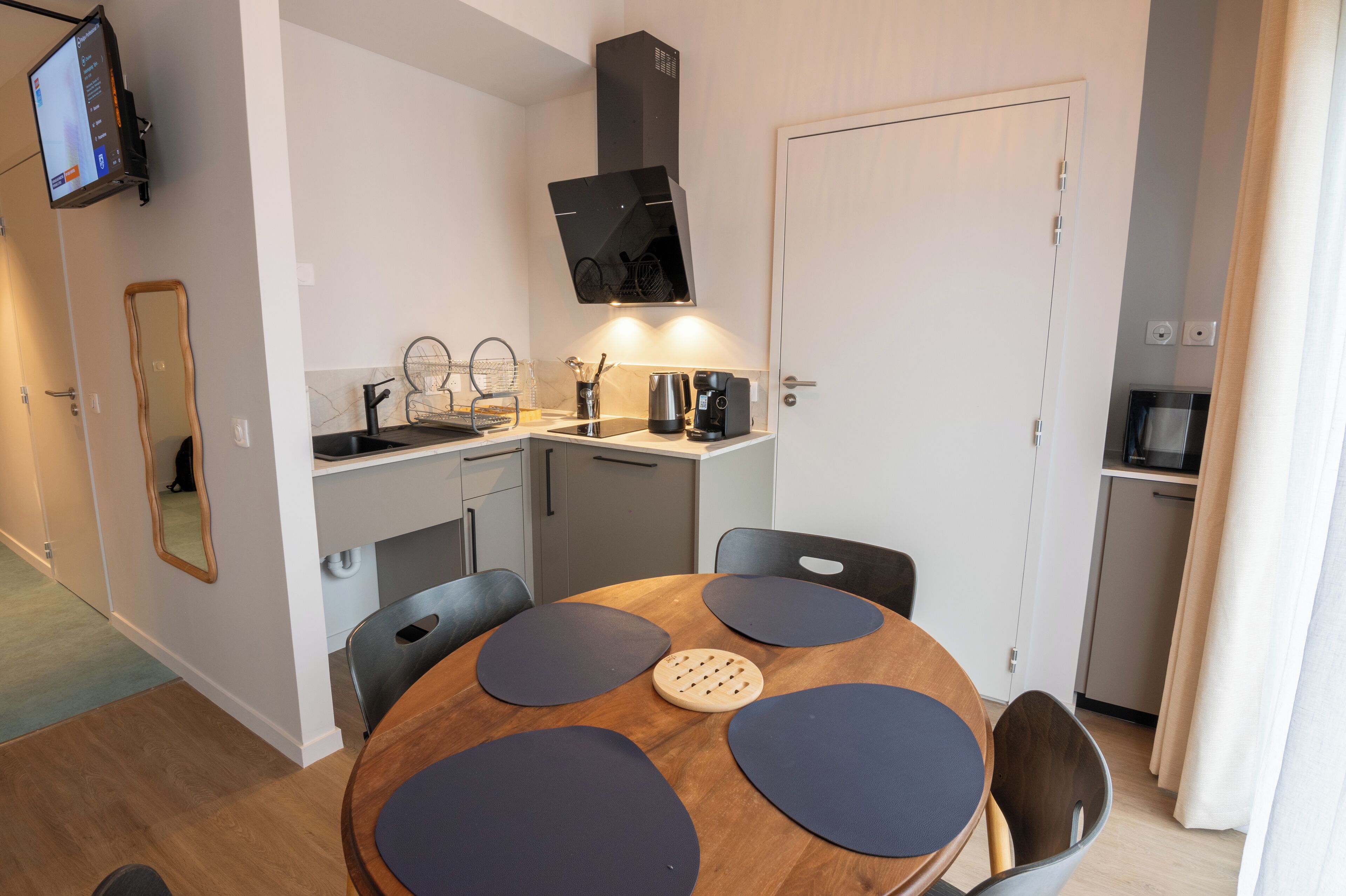 A compact kitchen with a round dining table, a built-in oven, and a TV mounted on the wall.