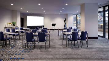 A conference room with a large screen, multiple tables, and chairs arranged for meetings.