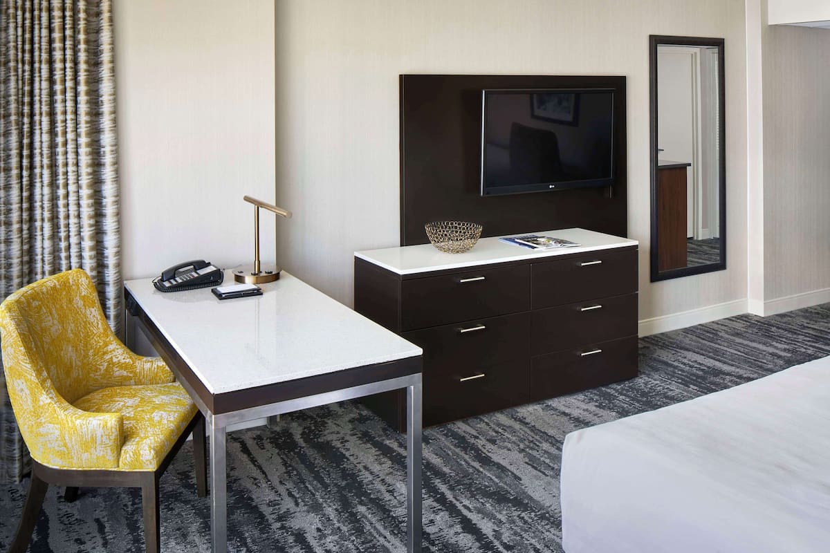 A hotel room with a bed, a desk with a chair, a television, a dresser, and a mirror.