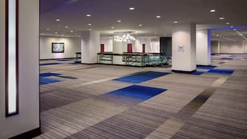 Un hall d’hôtel spacieux, doté d’un tapis à motifs, d’un espace salon central et d’un lustre moderne.