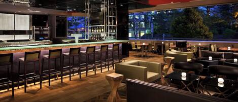 A modern bar area with a long counter, bar stools, and a variety of seating options including tables and chairs.