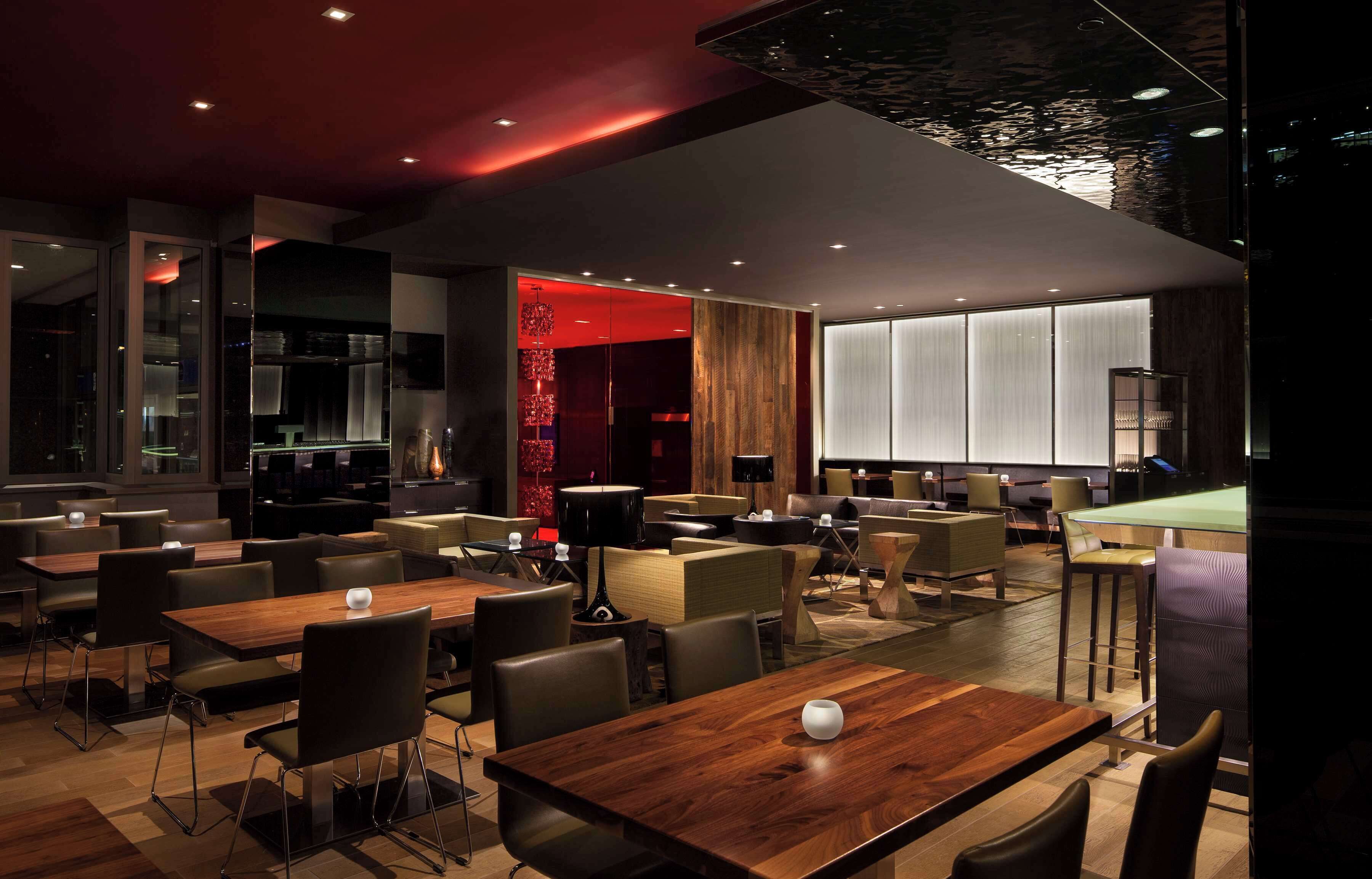 A modern restaurant with wooden tables and chairs, a bar area, and a large window providing natural light.