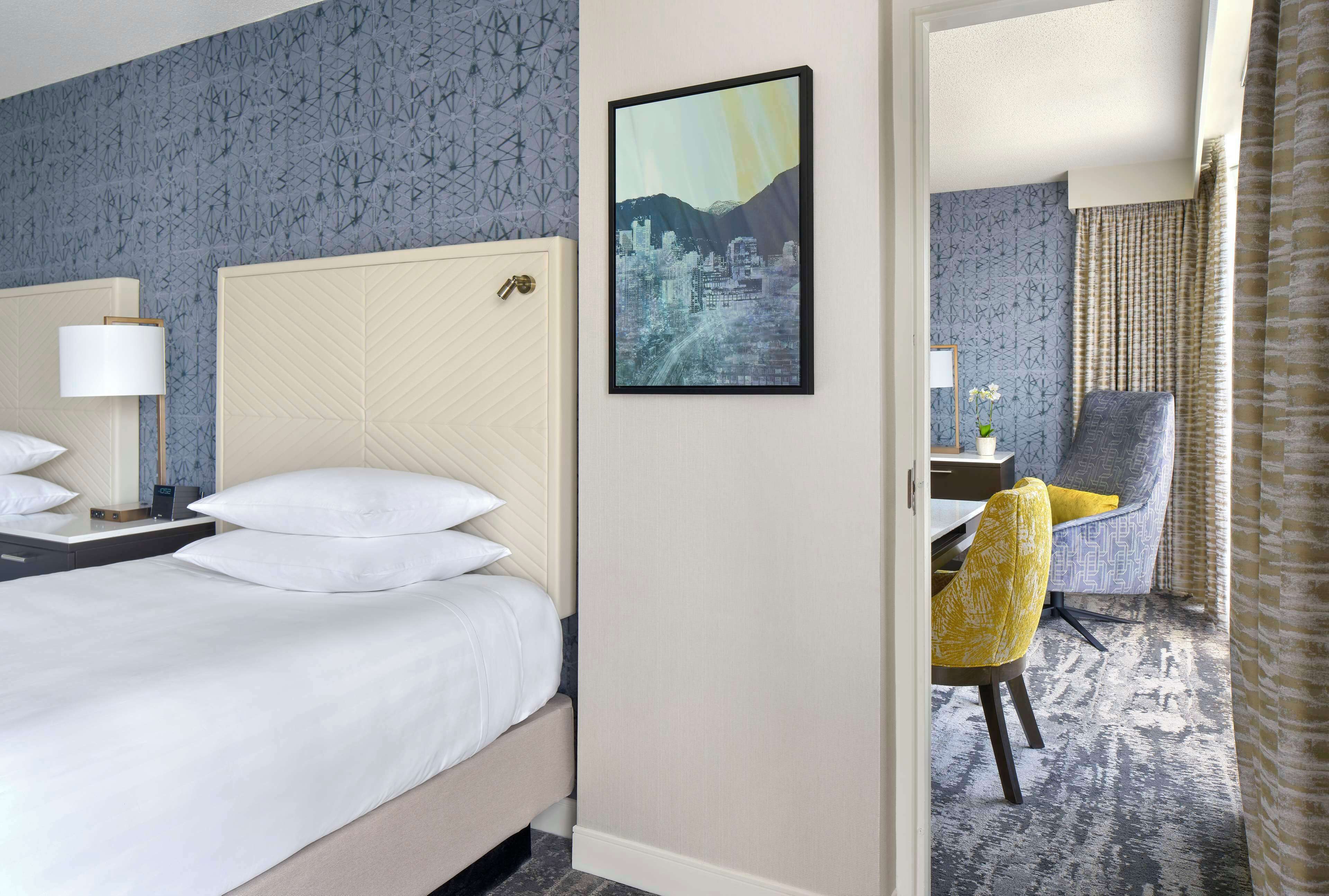 A hotel room with a bed, a chair, a desk, and a framed picture on the wall.