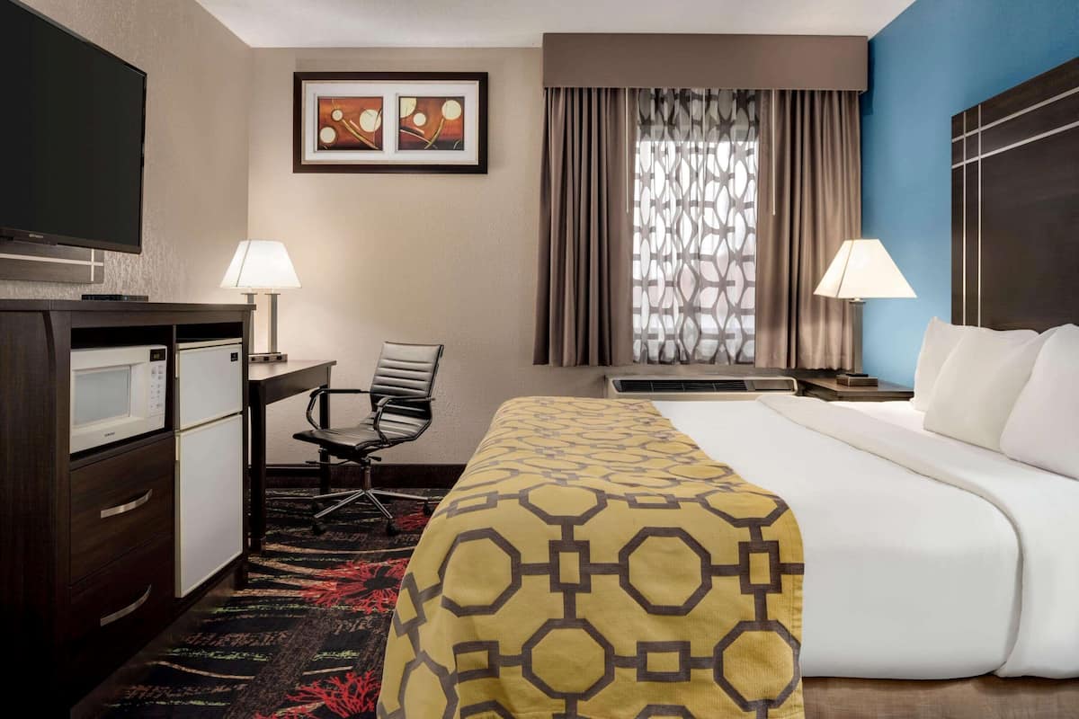 Habitación de hotel con cama, escritorio, silla, televisor y ventana con cortinas.