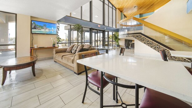 Eine großzügige Lobby mit modernem Design, inklusive einer Holztreppe, einer gemütlichen Sitzecke mit Sofa und Sesseln sowie einem großen Flachbildfernseher an der Wand.
