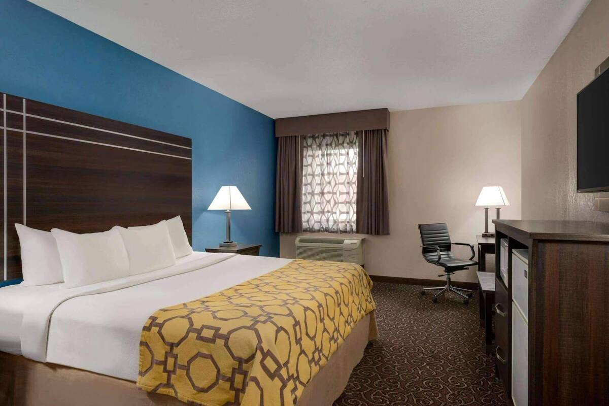 Habitación de hotel con cama, dos lámparas de noche, un escritorio con silla, televisor y ventana con cortinas.