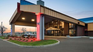 Ein modernes Hotel mit überdachter Eingangsparte, Parkplatz und angelegter Grünfläche.