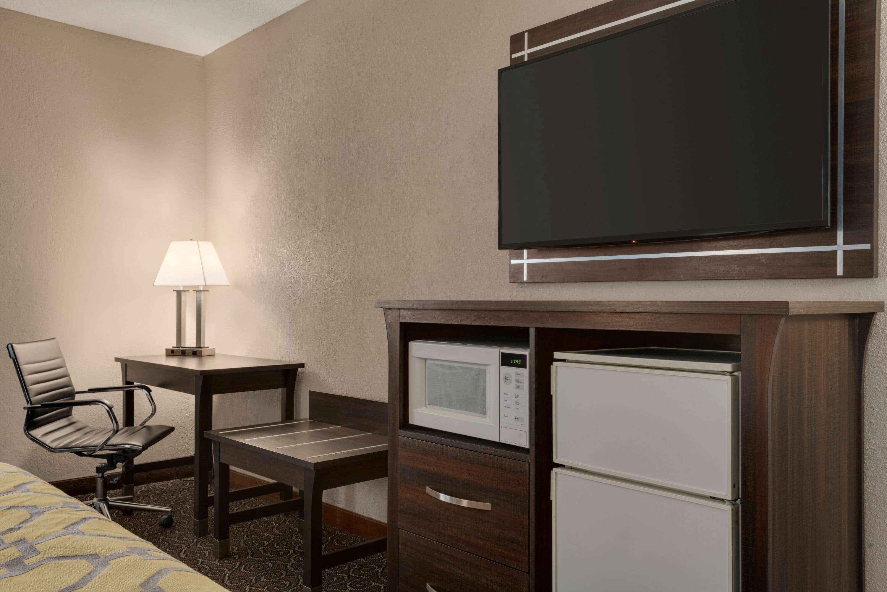 Habitación de hotel con cama, escritorio con lámpara, televisor y minibar.