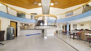 Eine großzügige Lobby mit einer zentralen Treppe, einem Empfangsbereich und einem Essbereich mit Tischen und Stühlen.
